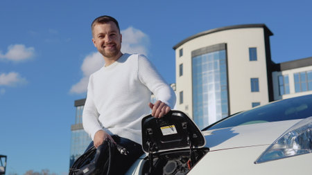 A fair-skinned male driver holds a charging cable for an electric carの写真素材