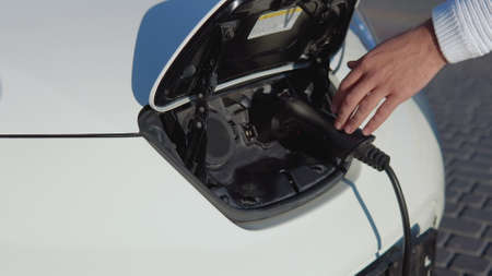 A fair-skinned male driver disconnects the electric car from the power system. Close-up viewの写真素材