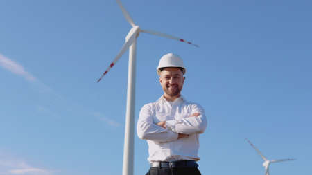 Air power engineer stands in business style clothes and white helmet on a background of windmillの写真素材