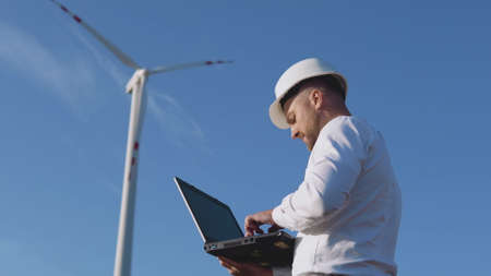 A male engineer in a white helmet and a classic shirt inspects the power plants capacity and makes notes in a laptopの写真素材