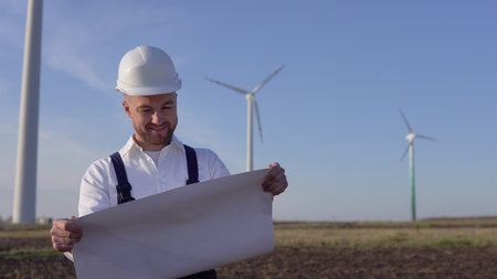 A male engineer in a white helmet and a classic shirt inspects the power plants capacity and reads...