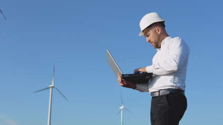 A male engineer in a white helmet and a classic shirt inspects the power plants capacity and makes notes in a laptopの写真素材