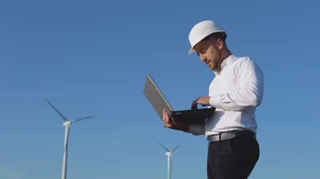 A male engineer in a white helmet and a classic shirt inspects the power plants capacity and makes notes in a laptopの写真素材