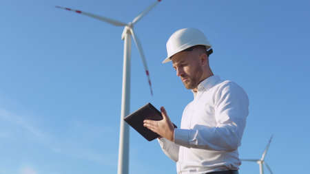 A male engineer in a white helmet and a classic shirt inspects the power plants capacity and makes notes on a tabletの写真素材