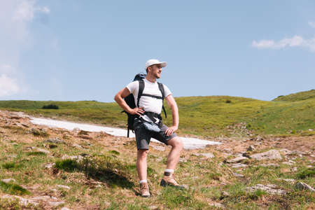 A bearded traveler with a backpack on the top of a mountain. A tourist with a backpack stands against the background of a mountainの写真素材