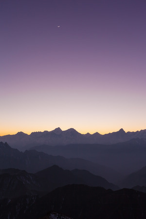 Panorama view of the twilight and moon in the sky with silhouette of mountains and cloudscape on top of Cattle Back Mountain (Niubeishan) in Sichuan Province, Chinaの写真素材