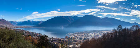 Stunning aerial panorama view of Locarno cityscape and Lake Maggiore from Madonna del Sasso church, snow covered Swiss Alps mountain and blue sky cloud in background in autumn, Ticino, Switzerlandの写真素材
