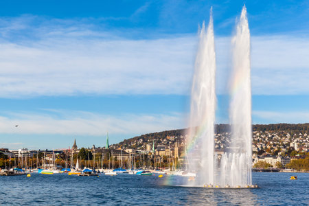 Beautiful view of the fountain at Mythenquai with rainbow in the Zurich lake and the cityscape of...