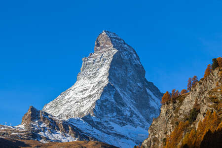 Stunning view of the famous Matterhorn peak of Swiss Alps from Zermatt valley on sunny autumn day with golden trees and grass in foreground, Valais, Switzerlandの写真素材