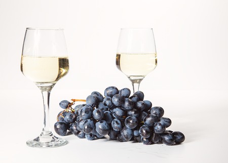 Two glasses and a bottle of white wine, on a white background near a handful of grapesの写真素材