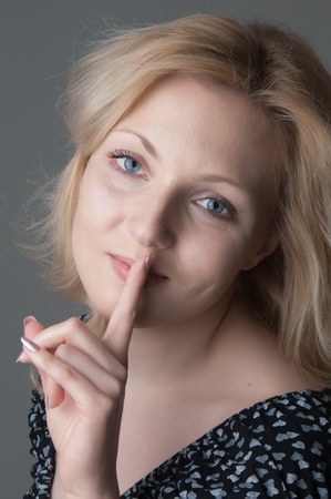 Portrait of young beautiful  blonde woman in  black dress with hearts puts her finger to her kips and looking at the camera close-upの写真素材