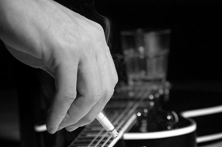 Composition of guitar and man's hand with cigarette smoking on black background