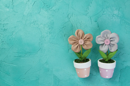 Beige and gray fabric flowers in flowerpots on turquoise textured background. Texture of concreteの写真素材