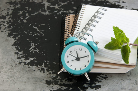 Turquoise alarm clock and notebooks on black gray  background. Copy space for text.