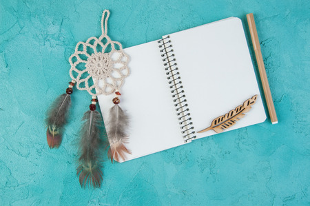 Top view of open blank notebook, mini beige dream catcher ,pencil  and wooden feather on aquamarine  textured background. Copy space for textの写真素材