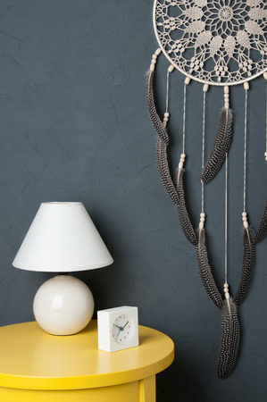 Beige crochet doily dream catcher ,yelioow nightstand , table lamp and alarm clock on dark gray textured background.の写真素材