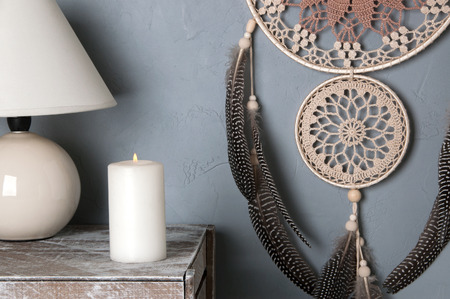 Beige brown crochet doily dream catcher, white candle and table lamp in bedroom interior on gray background. Copy space for text.の写真素材
