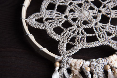 Beige crochet doily dream catcher close up on brown wooden background.