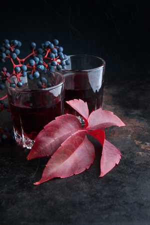 Two glasses of red drink and wild grapes with leaves on black background .Copy space for text.の写真素材