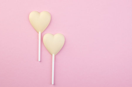 Two white chocolate candy hearts on a stick on pink background. Copy space for text.