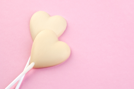 Two white chocolate candy hearts on a stick on pink background. Copy space for text.の写真素材