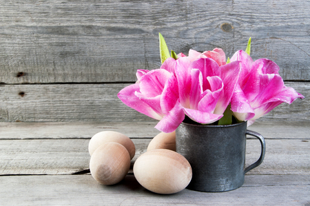 Pink tulips in vintage metal cup and wooden eggs on old wooden background. Copy space for text, Easter decorationsの写真素材