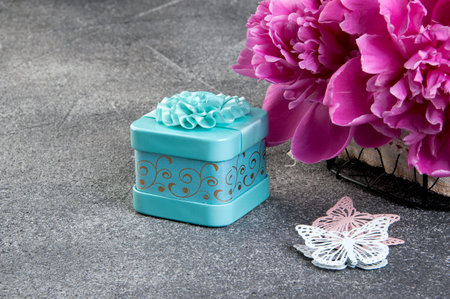 Pink peony, aquamarine gift box and butterflies close up on gray textured background. Texture of...