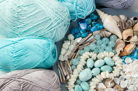 Knitting threads and gray plate with beads and seashells on shabby white wooden background. Copy space for text.の写真素材