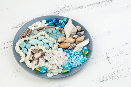 Gray plate with beads and seashells on shabby white wooden background. For marine design and copy space for text.の写真素材