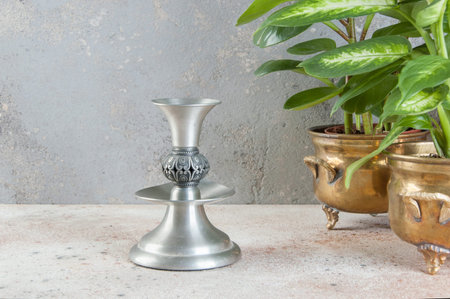 Vintage pewter candlestick and green plants in brass flower pots on concrete background. Copy space...