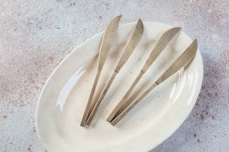 Old bronze knives on vintage oval plate on concrete background. Copy space for text, food photography props.の写真素材