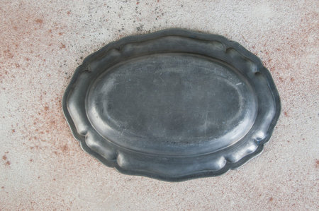 Antique pewter oval plate on concrete background. Copy space for text.