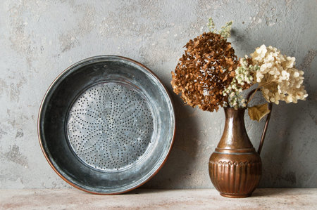 Antique copper sieve and composition of dried flowers in vintage copper jug on concrete background....