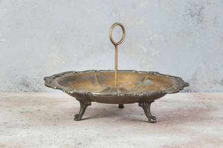 Antique brass serving dish with ring handle for desserts or appetizers with tea time on concrete background. Food photography prors and copy space for textの写真素材