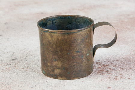 Old military brass mug with handle on concrete background. Copy space for text, photography props