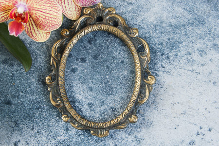 Antique brass empty picture frame and orchid flowers on concrete background. Photography props and...