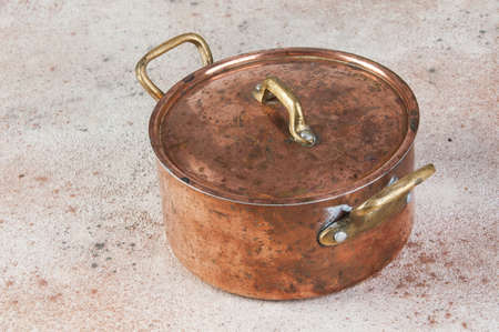 Old copper casserole with lid and brass handles on a concrete background. Copy space for text. Food photography props.の写真素材