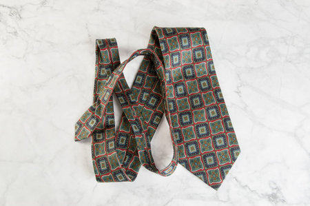Green neck tie with geometric pattern on marble background. Copy space for text.