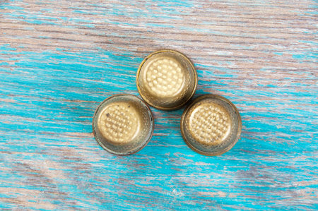 Three antique brass thimbles on wooden blue background. Copy space for text.