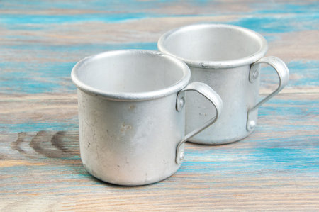 Two old aluminum mugs on wooden background. Copy space for text.