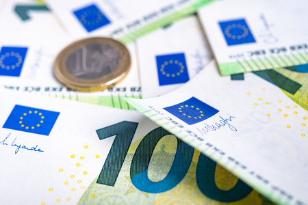 European unin cash. One euro coin lying on one hundred euro banknotes. Still life with lots of European Union flags.の写真素材