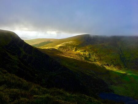 The setting sun shines through the hills and illuminates the valley in Irelandの写真素材