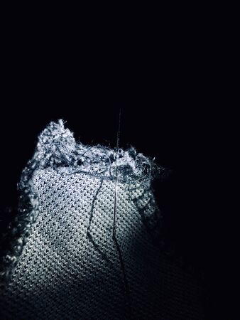 Close-up of needle with thread on silver canvas with black background.の写真素材