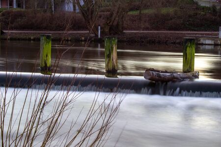 Wooden stakes stuck in a pond in the park. Blurred running water. Odense. Denmark.の写真素材