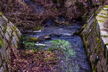 Small waterfall on a creek in winter paneled with branches and grass.の写真素材