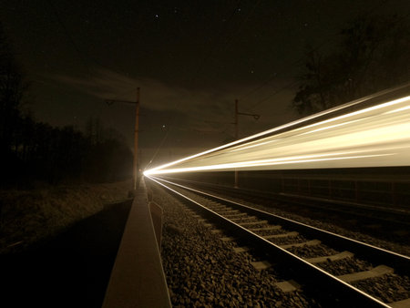 Focused night rails in the dark and blurry passing train. Night photo. Studenka. Czech Republic.