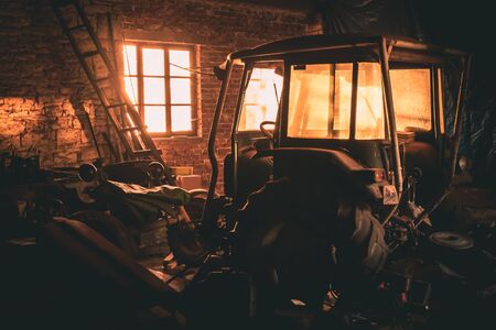 Old disassembled tractor in a brick workshop at sunset. The rays enter the buildingの写真素材