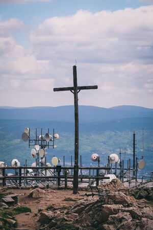 A large iron cross is contrasting with a telecommunication tower with multiple dish antennas. Czech Republicの写真素材
