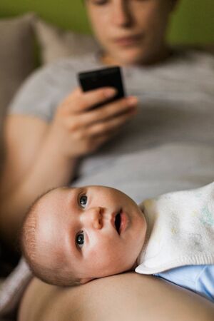 Mother using smart phone while holding baby in her lapの写真素材