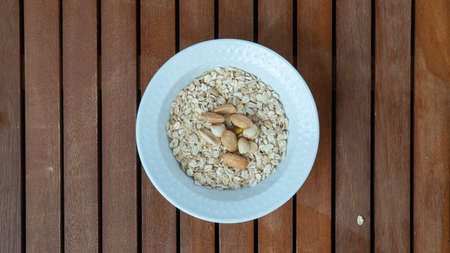 Dry oatmeal in a white plate with nuts on a wooden background view from aboveの写真素材